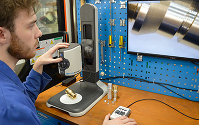 man in blue overall looking at monitor of magnified part using EVO Cam II digital microscope