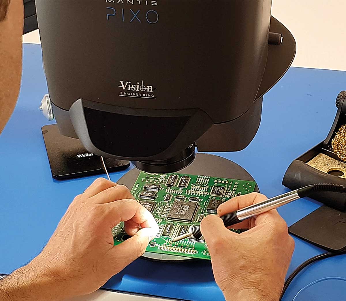 Woman soldering a PCB looking through Mantis stereo microscope